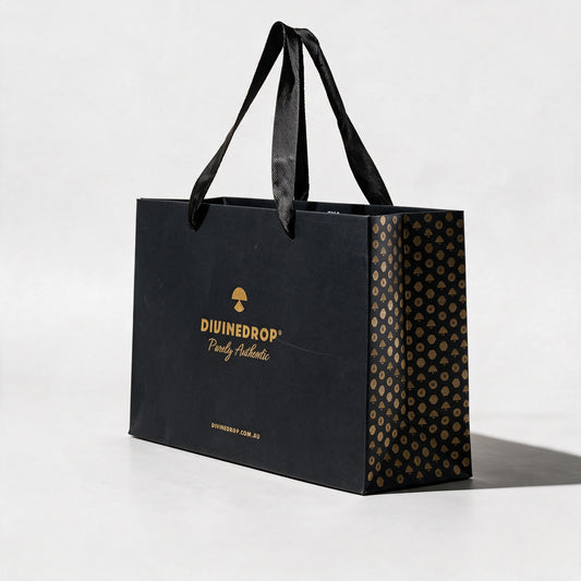 DIVINEDROP black gift bag seen from the side, showing the gold pattern side panel and black ribbon handles, on a light grey background