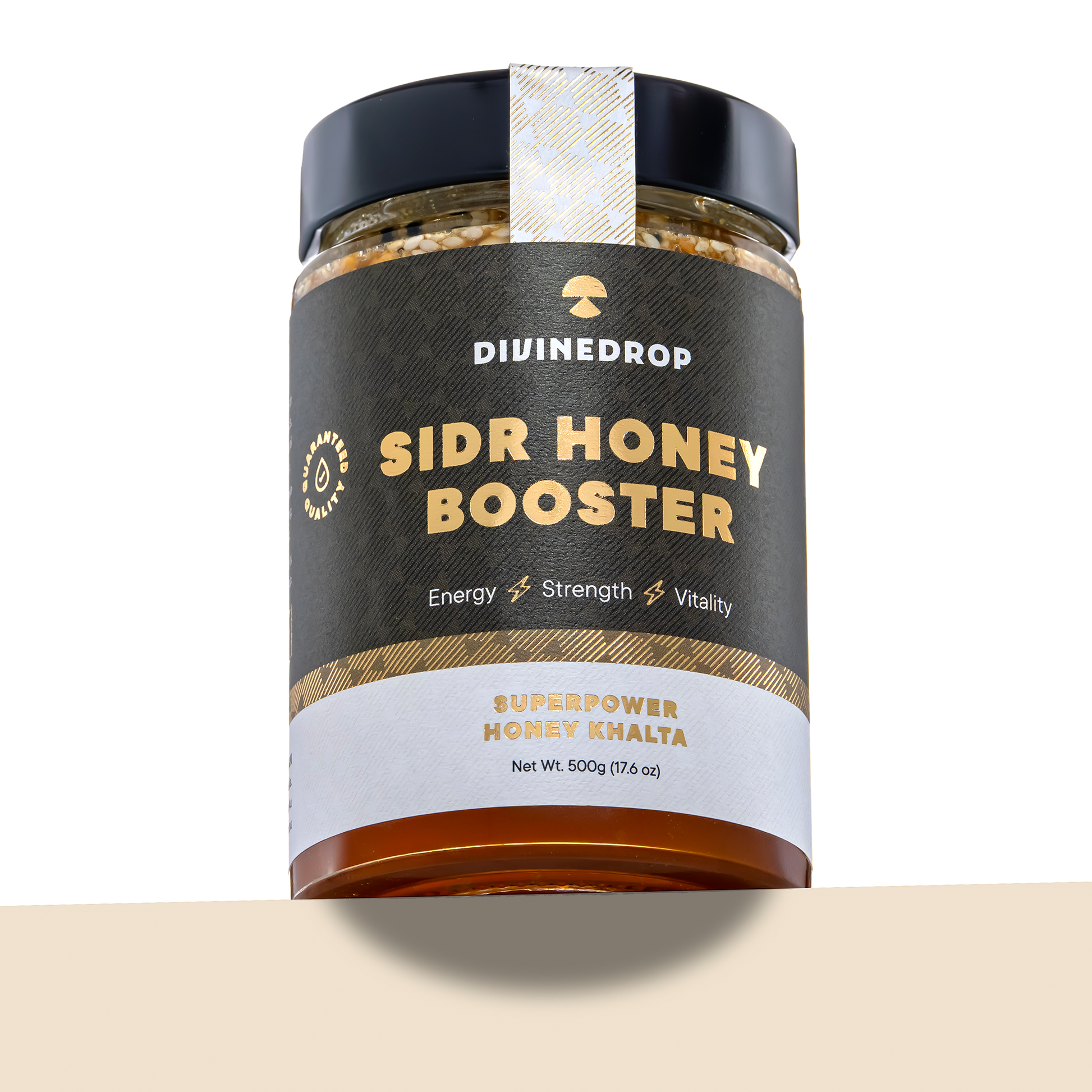 A jar of DIVINEDROP Sidr Honey Booster on a white background with a beige surface at the bottom. The jar has a black lid, a dark brown label with gold and white text, and a white seal on top.