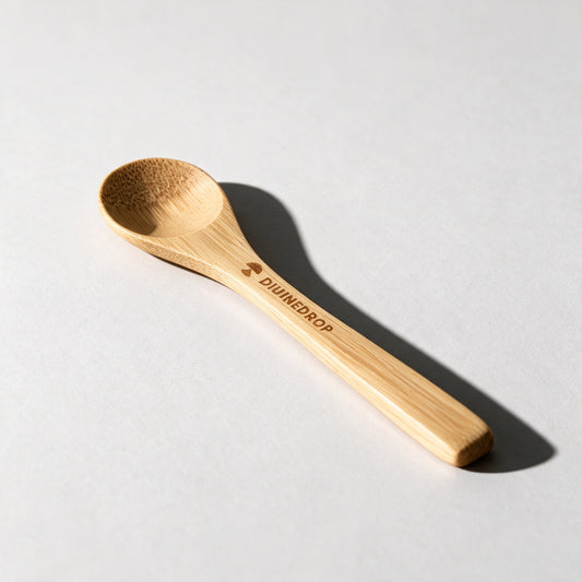 Bamboo honey spoon with the DIVINEDROP logo engraved on the handle, lying on a light grey background