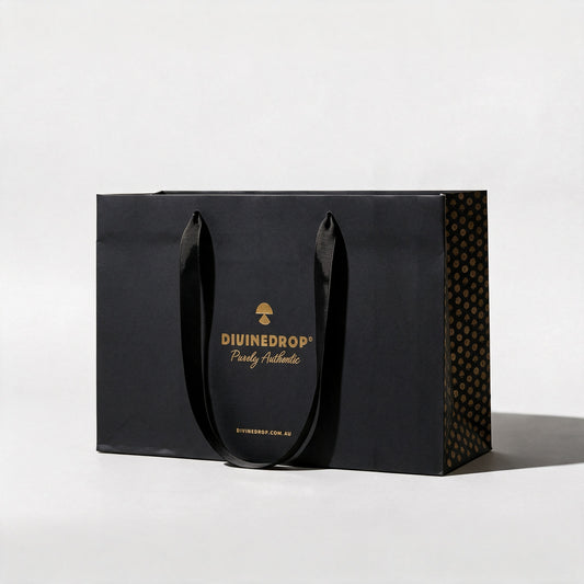 Black DIVINEDROP gift bag with gold foil logo, black ribbon handles and gold pattern side panel, on a light grey background