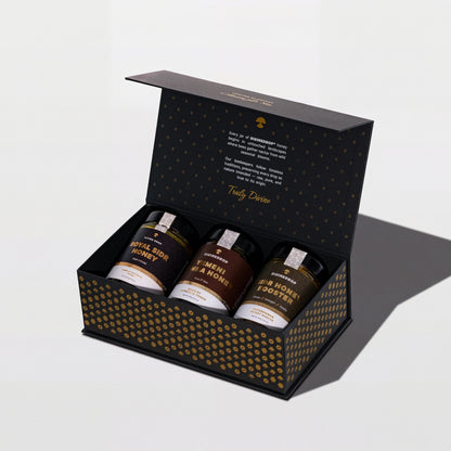 DIVINEDROP black gift box with gold pattern, open, holding three jars of Yemeni honey, on a light grey background