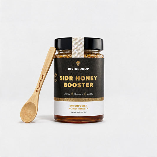 DIVINEDROP Sidr Honey Booster 500g jar with an engraved DIVINEDROP bamboo honey spoon, on a light grey background